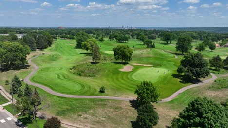 lush green golf course with players and pathways, city skyline in the distance