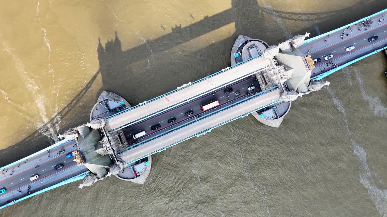 Incredible bird’s-eye aerial of London’s Tower Bridge as sunlight breaks through clouds, casting the bridge’s striking shadow onto the River Thames in a breathtaking cinematic reveal.
