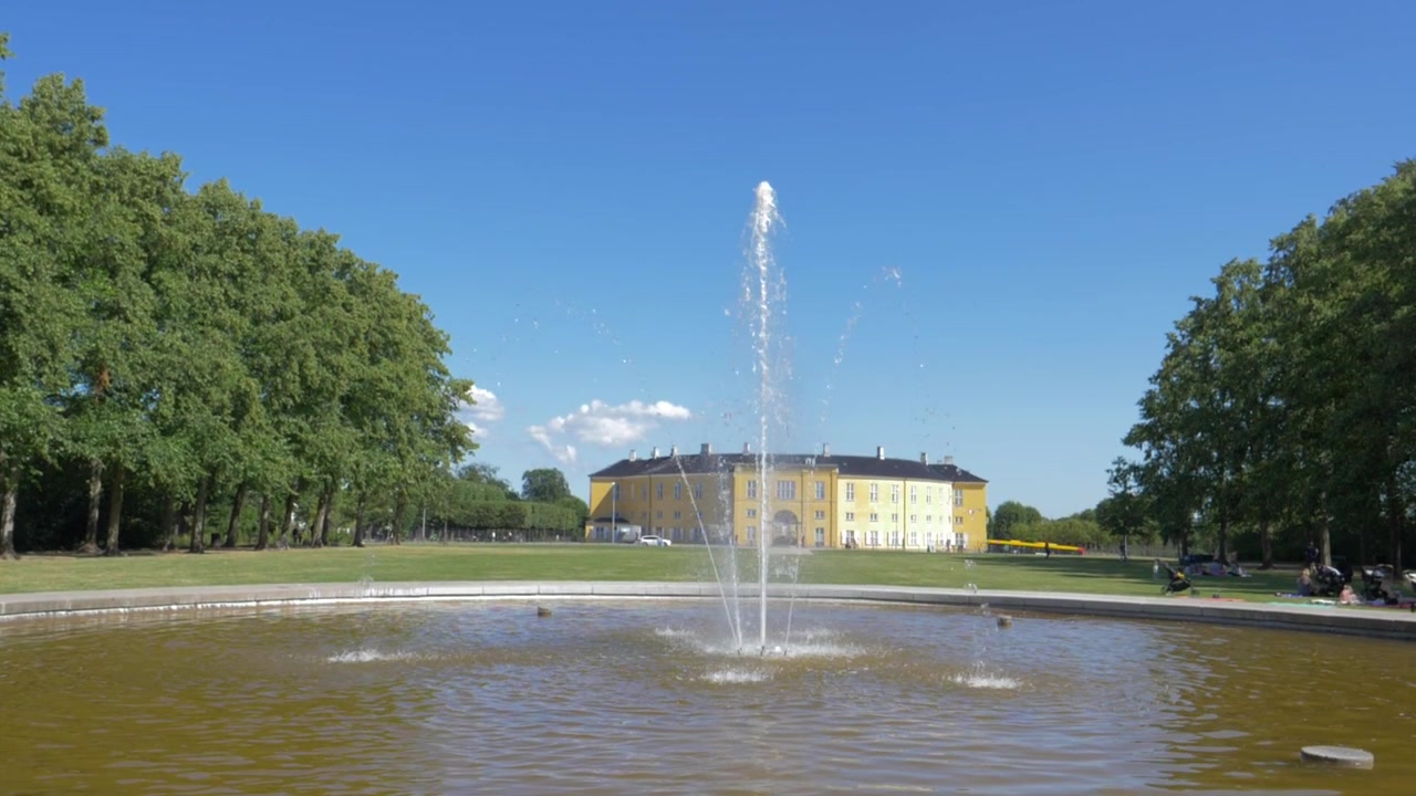 Un clip en cámara lenta de una fuente de agua en un parque verde con un castillo de fondo.