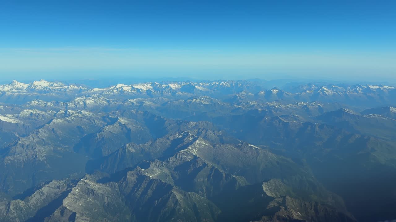 An Aerial elevated view of the Swiss Alps Mountains taken from a jet cockpit crossing the Alps in a hazy summer morning wth almost no snow.