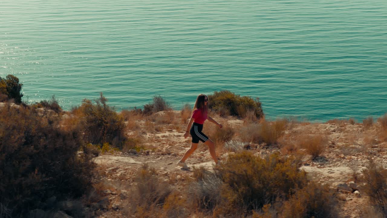 Young woman walking on a mountain trail with the view of the sea as a background