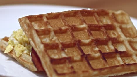 Waffles-made-into-a-breakfast-sandwich-with-scrambled-eggs,-bacon-and-cream-cheese-rotating-on-a-plate