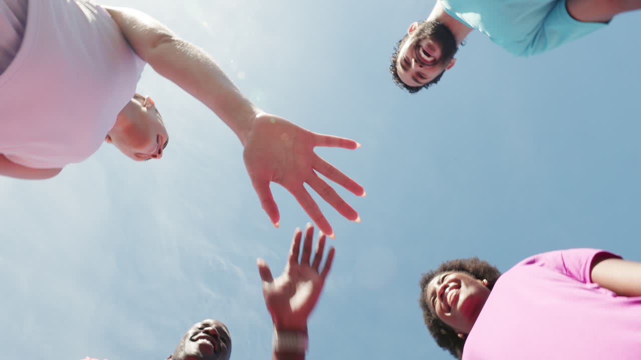 Diverse Group of Friends Stacking Hands and Cheering Under Blue Sky