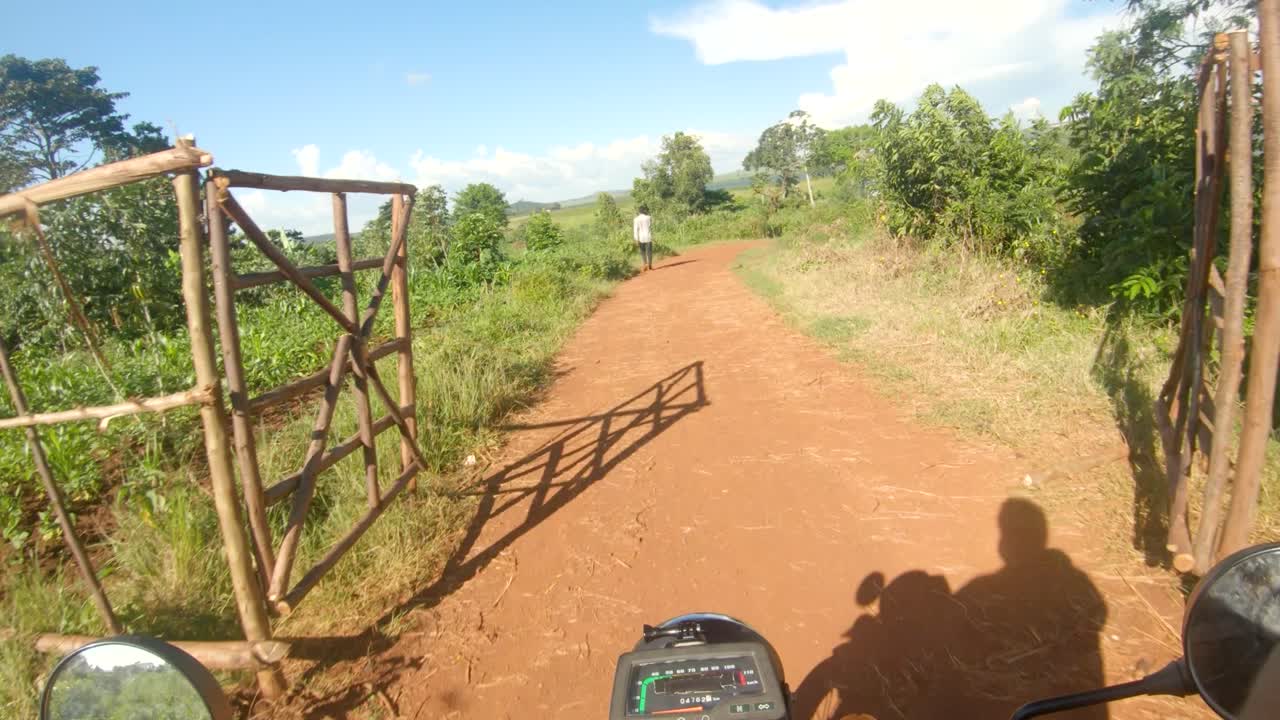 toma de punto de vista de un hombre blanco que se aferra a los manillares de una moto y recorre el áfrica rural