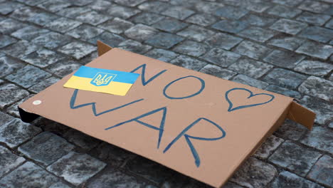 antiwar cardboard sign with ukrainian flag on cobblestone pavement