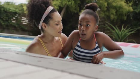 happy african american mother and daughter playing in swimming pool in garden, slow motion