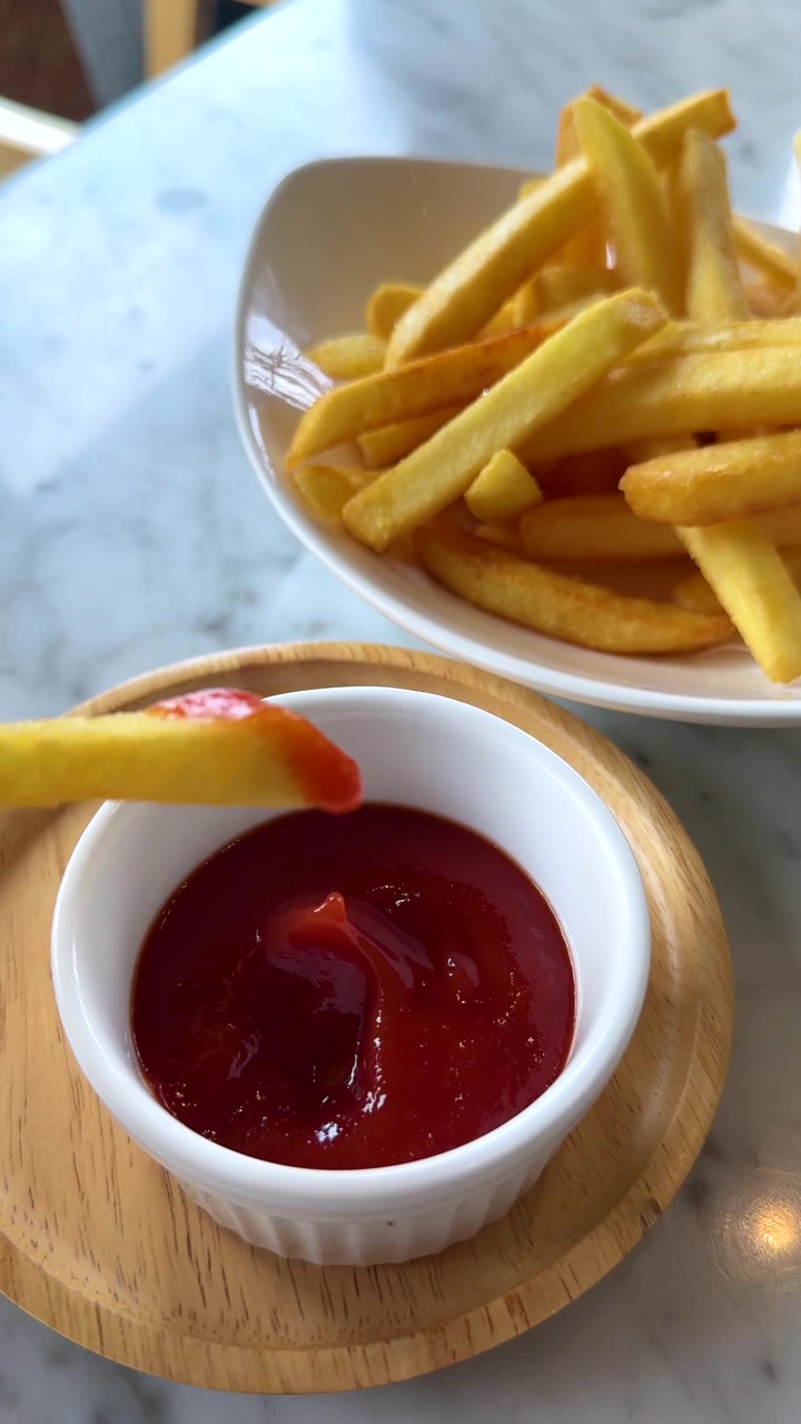 Primo piano dall'alto di una mano che intinge una patatina fritta croccante nel ketchup di pomodoro rosso.