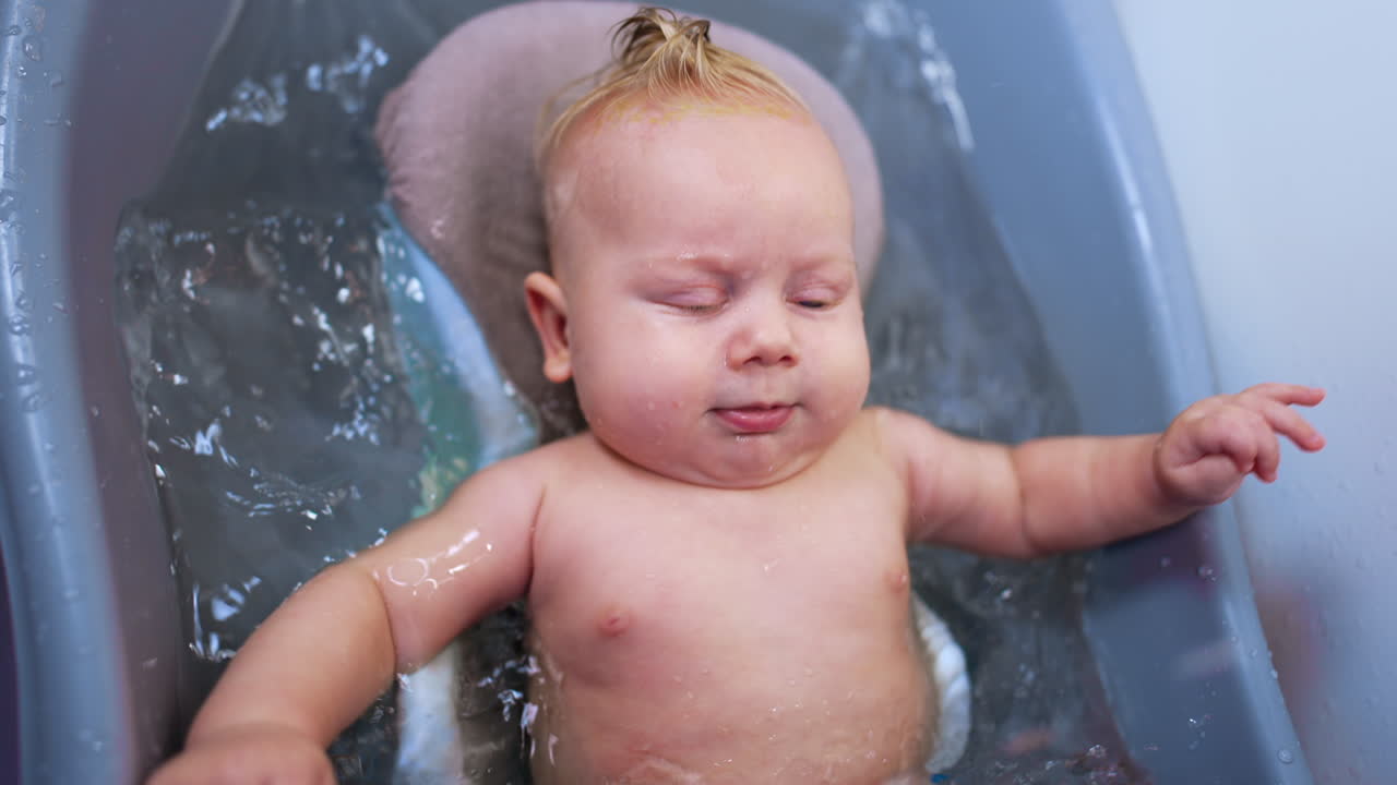 Lovely infant baby lies relaxed in the bath. Cute plump child waving hands and feet actively in water.