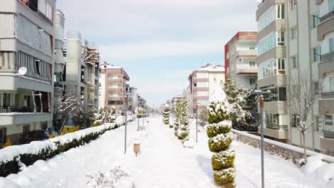 low-to-high drone-like shot on a cloudy day in denizli, turkey, with snow-covered landscape, apartment buildings on both sides, and a pedestrian walkway resembling a park in between