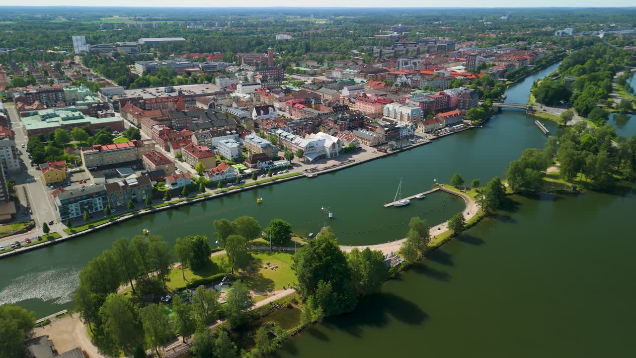 Hoge luchtopname toont het stadsbeeld van Trollhättan langs de Göta Älv rivier met het eilandpark Spikön, een zeilboothaven, kleurrijke daken, kerktorens en een brug in de zomer.