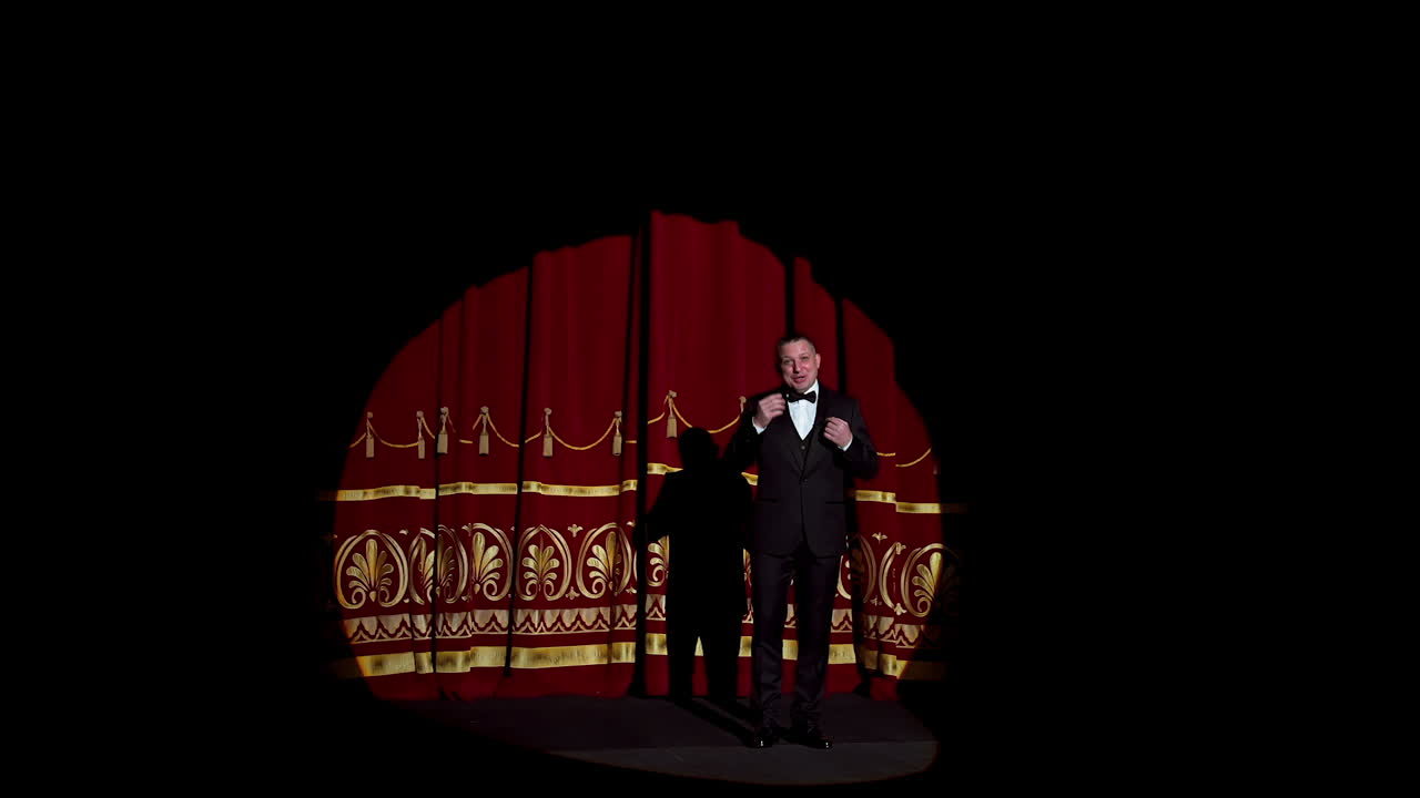 Announcer on a stage in theater. Bright round light on one person. man in black suit performs to the auditorium.