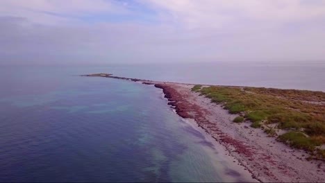 Aerial-pass-out-along-sandy-spit-towards-ocean-horizon