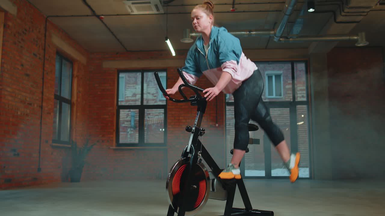 Athletic woman riding on spinning stationary bike training routine in haze gym weight loss indoors