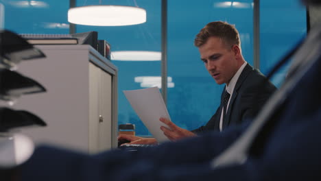attractive-businessman-reading-documents-in-busy-office-executive-working-late-on-company-project-deadline