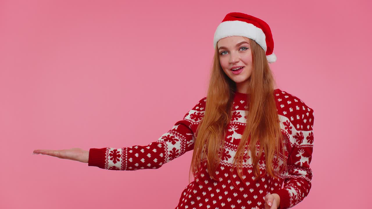 여성은 빨간 새해 스웨터를 입고 사이 엄지손가락을 올리고 빈 광고 공간을 가리키고 있습니다.