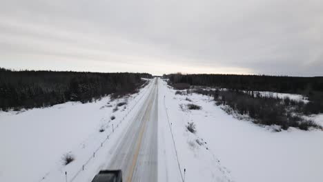 A-Cinematic-Black-Offroad-Pickup-Truck-Car-Driving-Under-Drone-Shot-on-a-Winter-Snow-Covered-Highway-Road