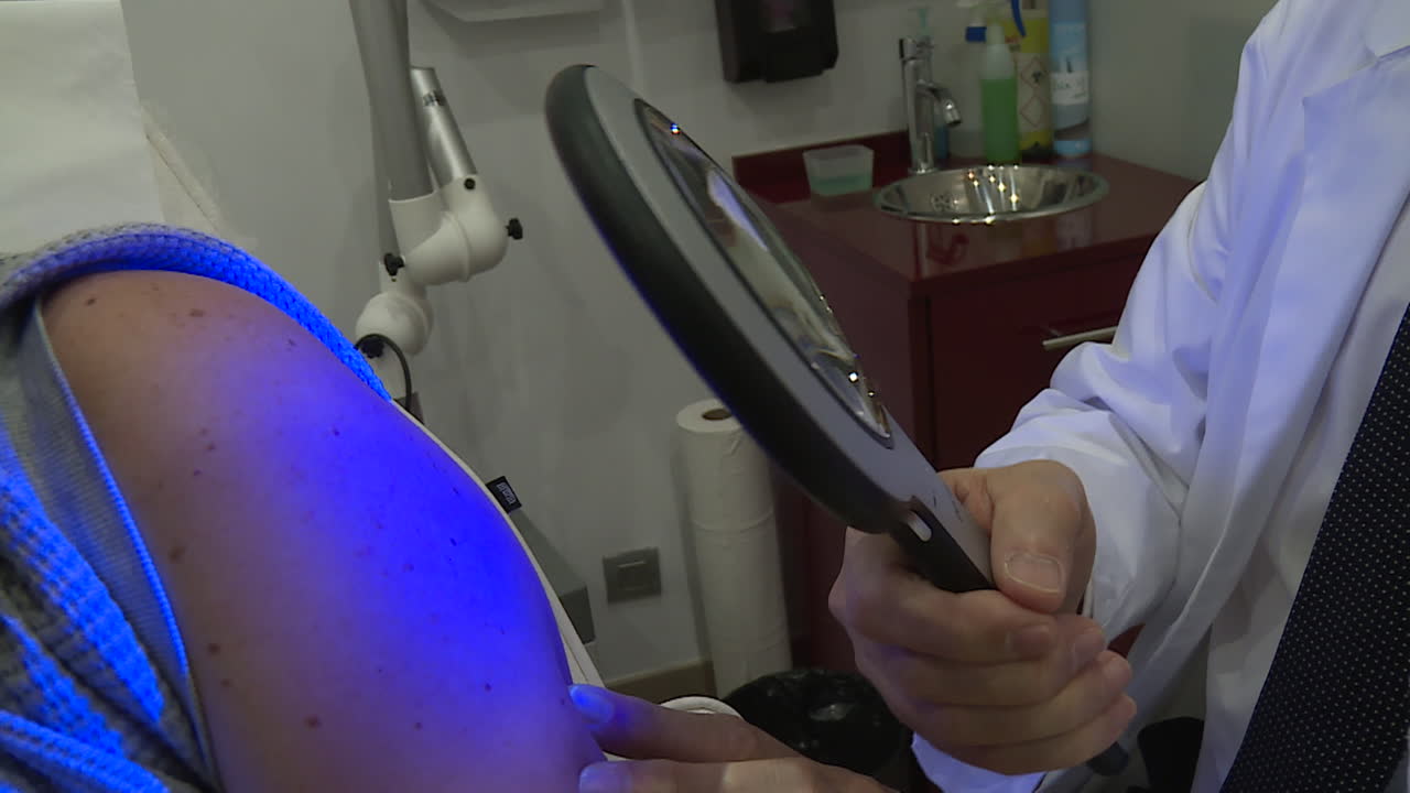 Dermatologist examining patient's skin lesion using magnifying glass and UV light