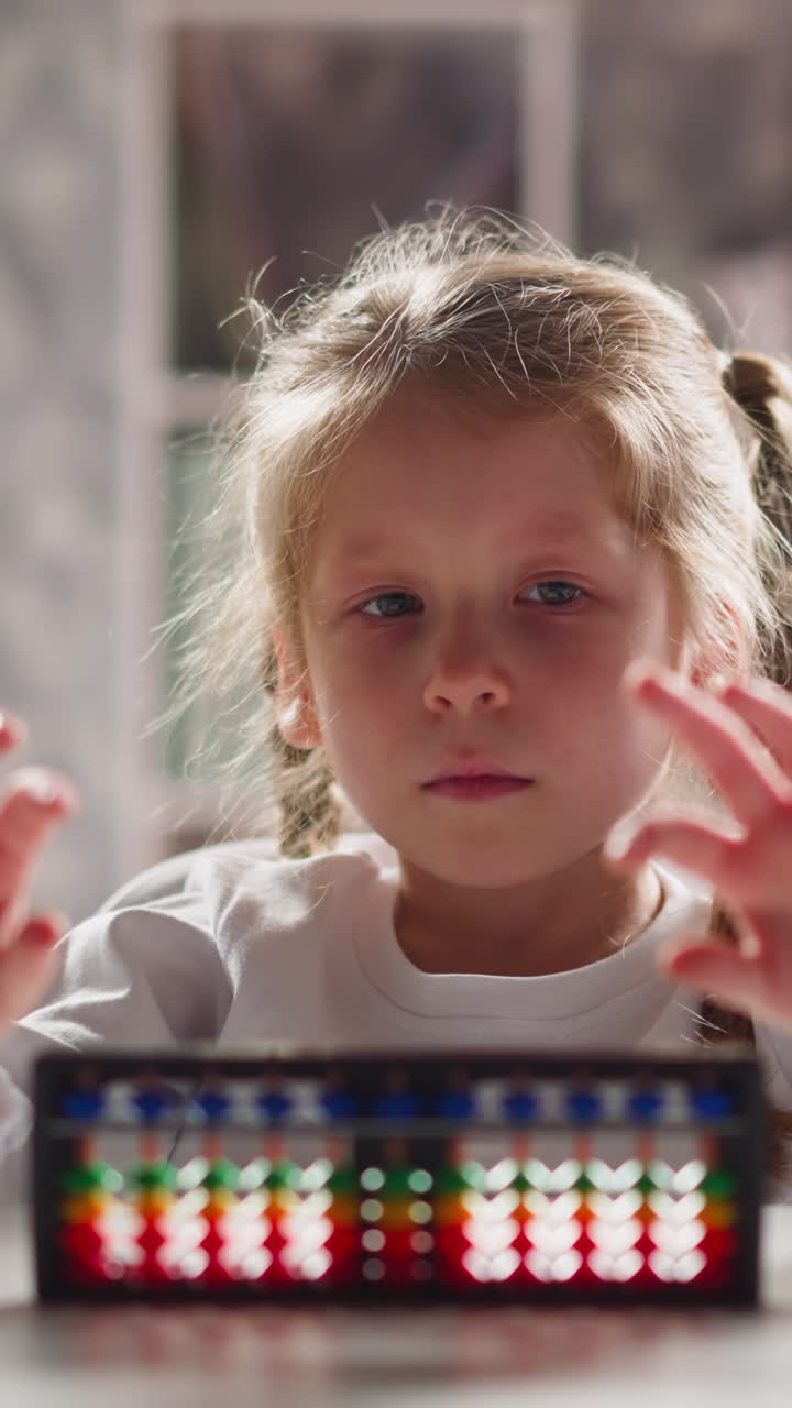 Pretty little girl student with toy abacus does gymnastics for fingers sitting at table during maths lesson in kindergarten close view slow motion