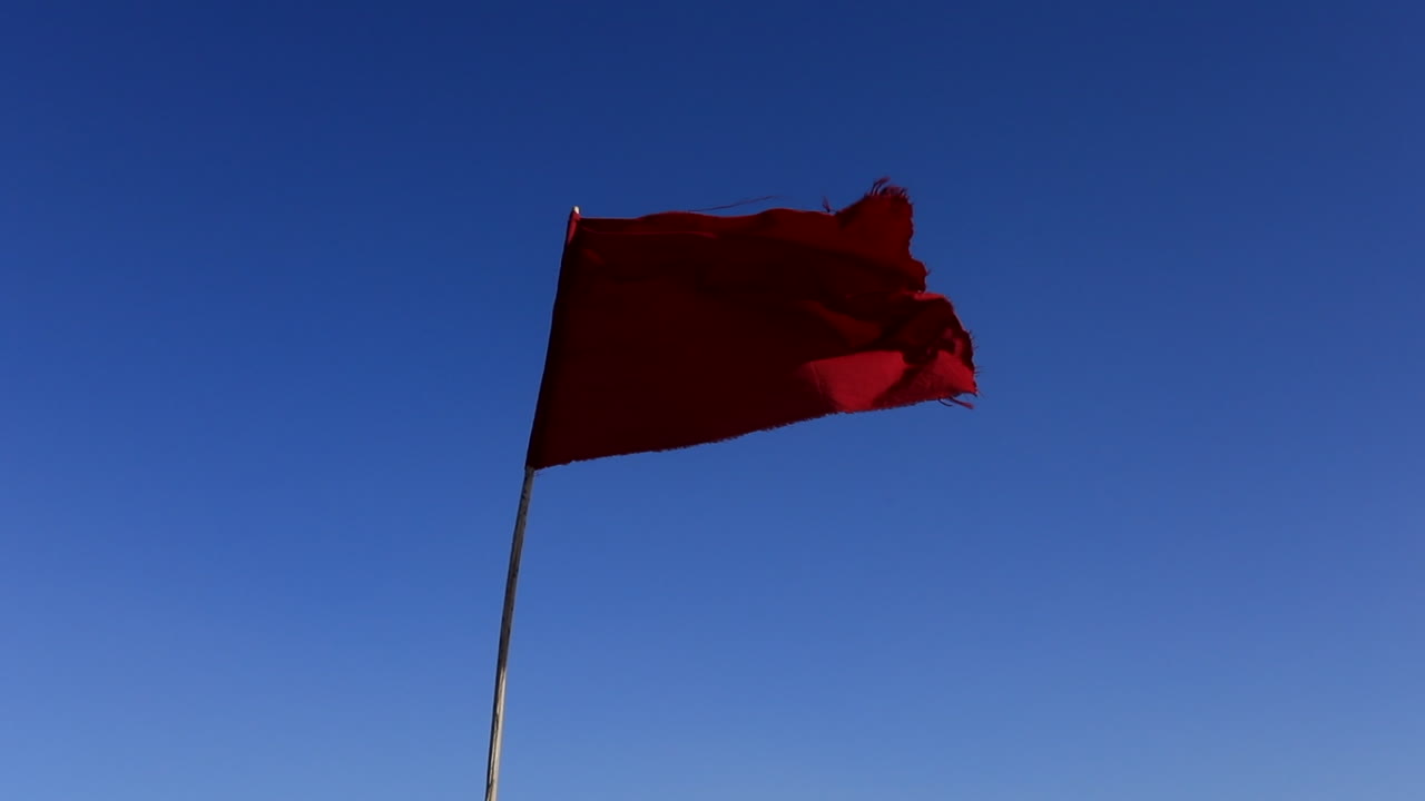 bandera roja revoloteando contra el cielo azul claro en el desierto de sal de túnez, chott el jerid, símbolo de precaución