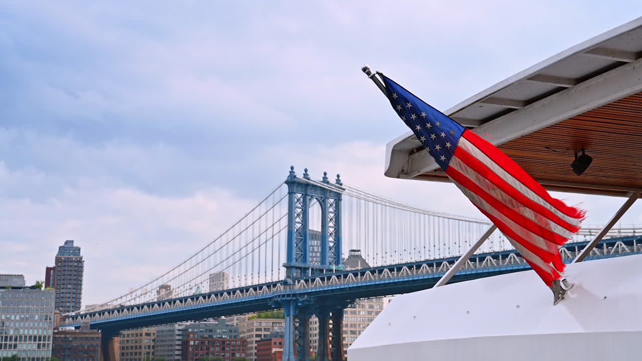 Vista della bandiera americana vicino al ponte della città. Una bandiera americana sventola da una barca, mostrando lo skyline e il ponte di una città durante il giorno