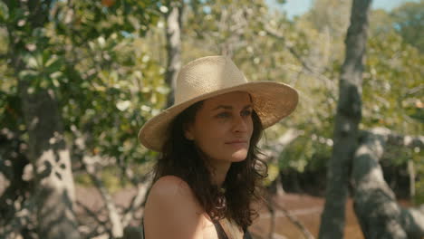 primer plano en cámara lenta de una mujer europea morena feliz con un sombrero de paja mirando un bosque verde