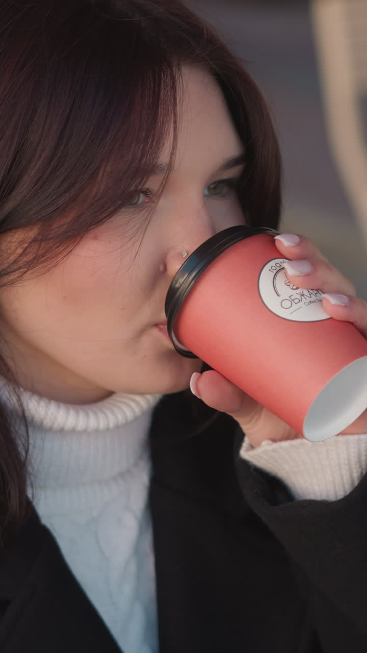 Freelancer sips coffee, gently placing the cup back down on the table, with a blur of wooden chair and flowers in the background as she takes a break from work in a cozy outdoor space