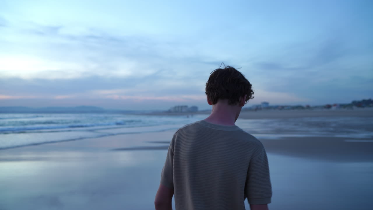 Contemplative teenager walking barefoot on wet, glistening sand near ocean shoreline during mesmerizing sunset, embodying peaceful solitude and quiet reflection
