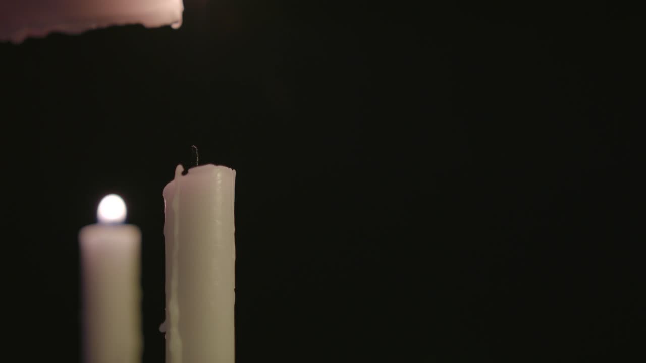 Una candela bianca che accende due candele bianche al rallentatore.