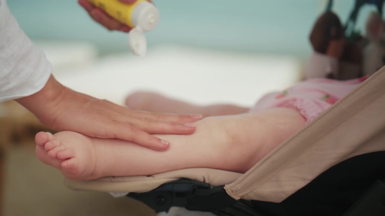 Primo piano di una madre che applica la crema solare sulla pelle di un bambino in spiaggia durante una giornata di sole.