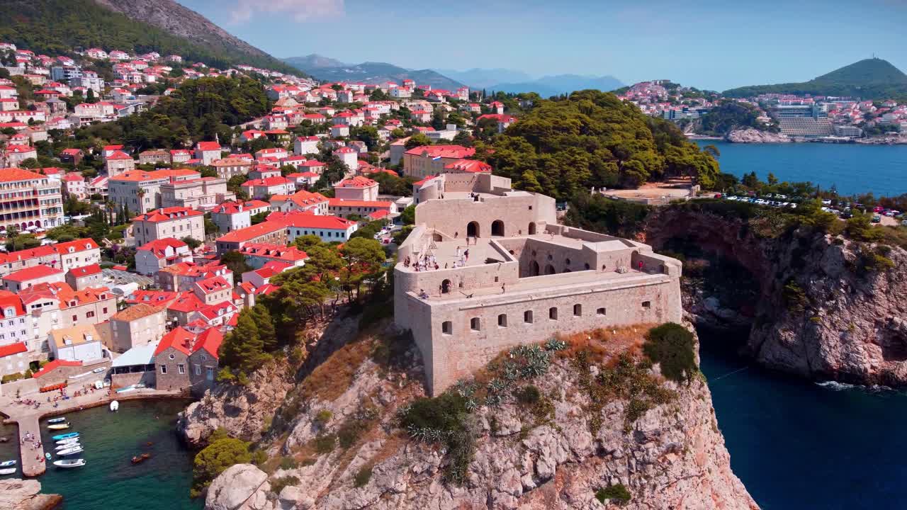 Letecký pohled dronem na pevnost Lovrijenac tyčící se na skalnatém útesu nad Jaderským mořem v Dubrovníku, Chorvatsko, s historickými kamennými zdmi, červenými střechami a bujnou pobřežní krajinou
