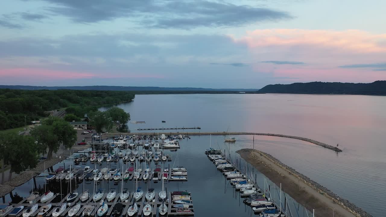 Aerial view of a peaceful marina at sunrise, with multiple boats docked along the shore, reflecting the soft colors of the early morning sky on the calm waters