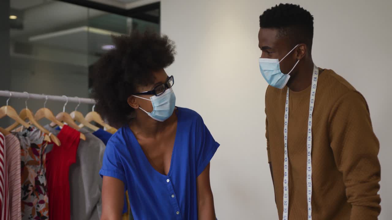 African american male and female fashion designers wearing face masks in discussion at work