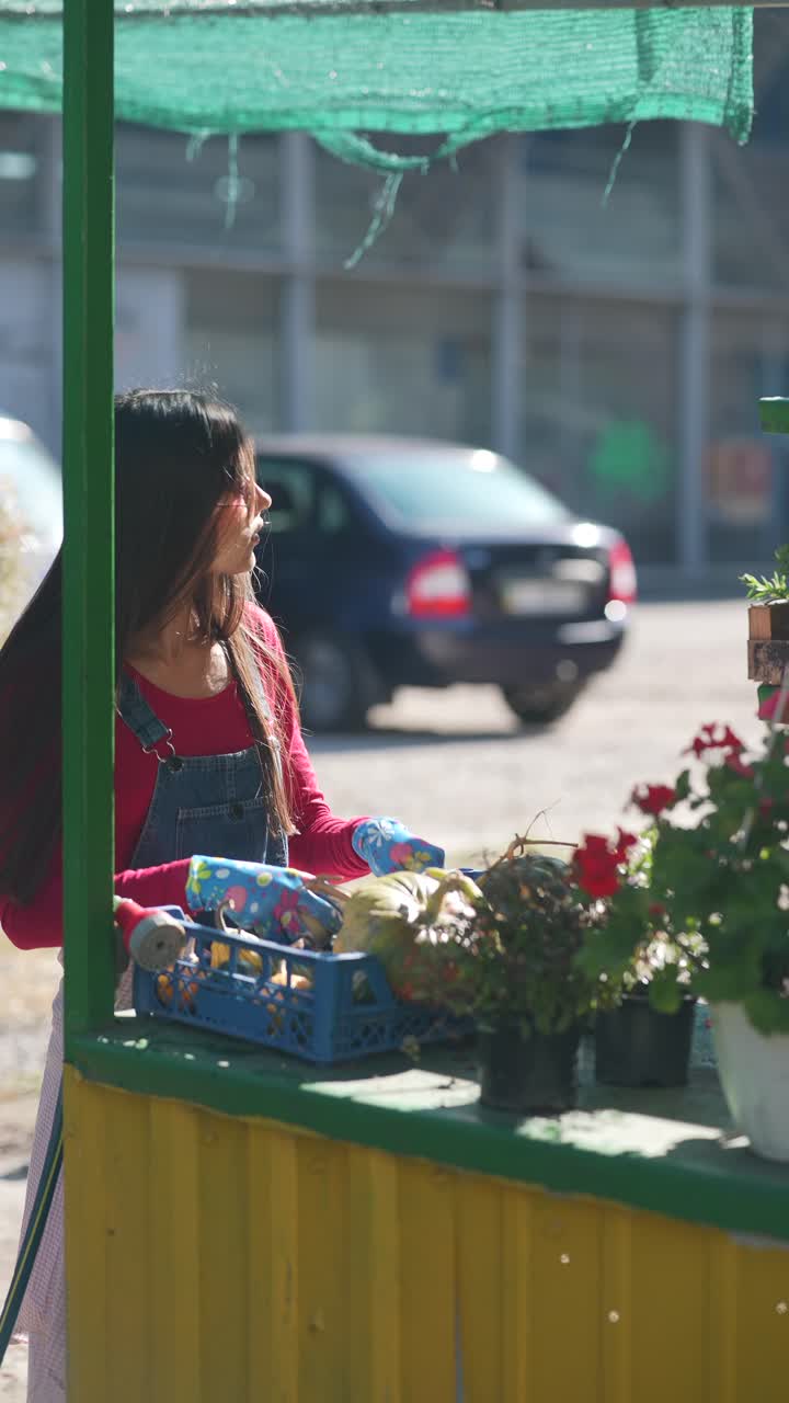 mujer joven vendiendo productos y flores en un mercado al aire libre