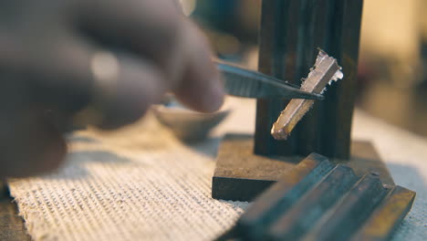 jeweler takes gold bar with tweezers on table close view