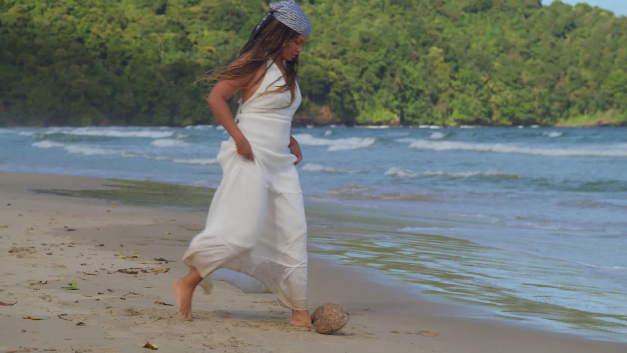 una joven vestida de playa patea un coco en la playa