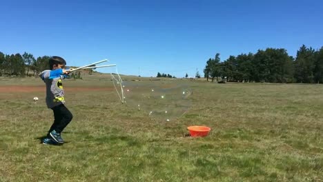 niño chico haciendo pompas de jabón gigantes al aire libre