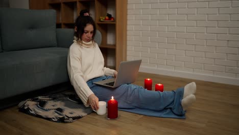 young woman working on modern laptop while sitting in a cozy room around candles