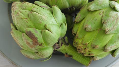 Whole-fresh-artichokes-on-plate,-rotate.-Closeup