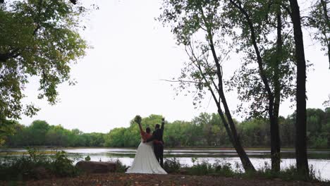 unrecognizable newly wed couple raising arms up, celebrating marriage outdoors in forest by river