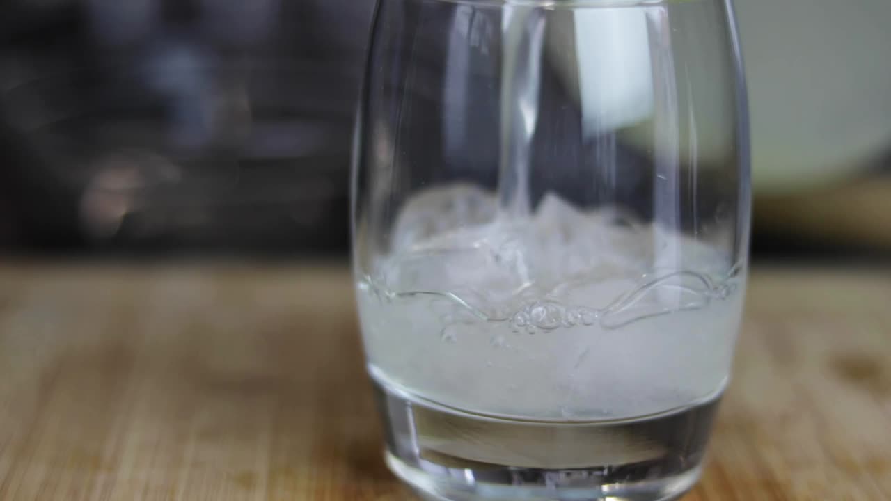 나무 판자에 앉아 있는 얼음이 들어 있는 유리잔에 레모네이드를 붓는 슬로우 모션 샷