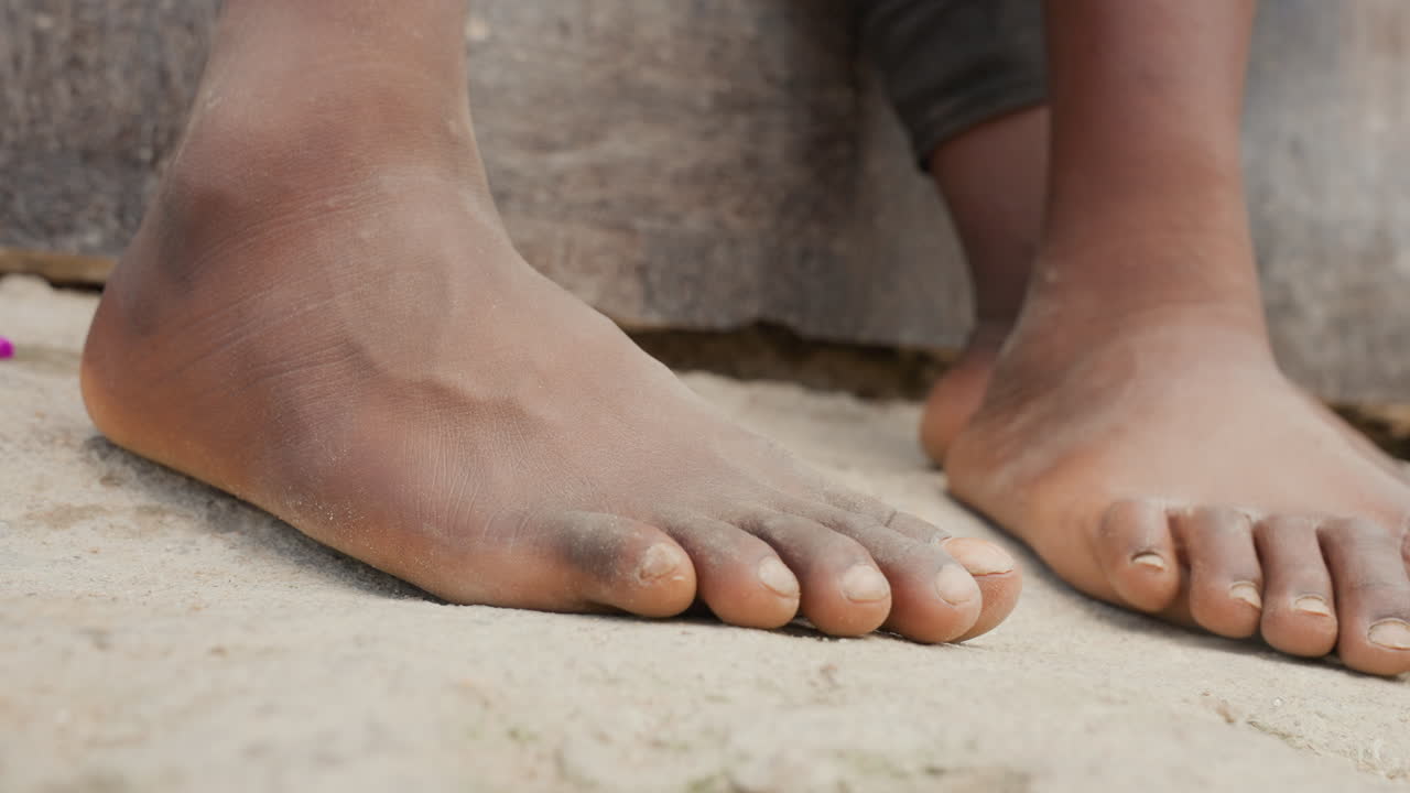 Bambini piccoli seduti pacificamente su una superficie di sabbia soffice. Bambini che si rilassano tranquillamente su un terreno sabbioso dopo aver giocato all'aperto. Bambini giovani che si godono un momento tranquillo a piedi nudi su un paesaggio sabbioso sereno.