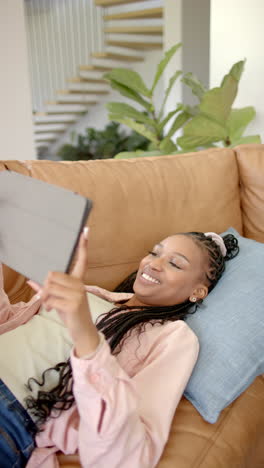 vertical video: relaxing on couch, woman smiling while using tablet at home