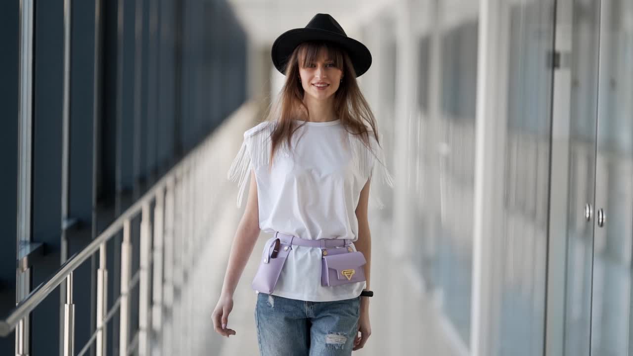 hermosa chica en un sombrero con un modelo de microbag en la cintura caminando por los pasillos de vidrio