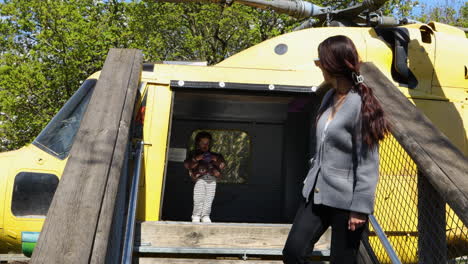 a woman and a child walking out of a yellow helicopter at battersea zoo, london