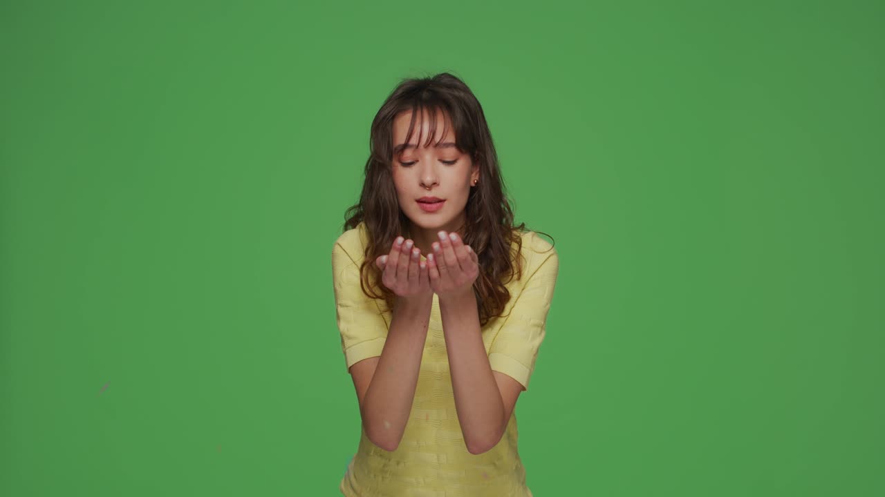 행복한 젊은 예쁜 소녀, 휴일을 축하하라, 손바닥에서 반이는 콘페티를 불어넣어, 크로마키 녹색 배경에 축하해