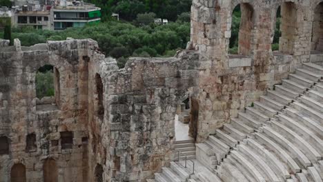 rising view of the steps and seats of the ancient roman theater odeon of herodes atticus on filopappou hill in greece, showing trees and athens buildings in the background