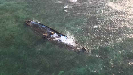 drone aerial moving around a shipwreck in the ocean with waves crashing into it during sunset