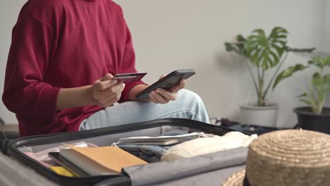 woman using smartphone and credit card payment getting ready for travel, packing clothes and accessories in suitcase. concept of traveling, adventure.