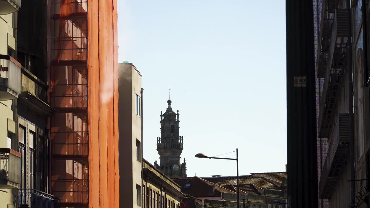 4k construcción de un edificio en el centro de la ciudad de oporto con la torre clerical al fondo, algo de polvo saliendo de las protecciones de la fachada