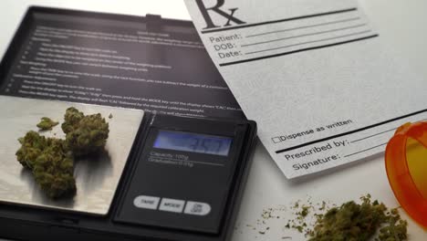 a digital scale measures grams of marijuana, next to a prescription note and open pill bottle spilling a small pile of marijuana